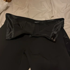 Svarta kostymbyxor - Snygga svarta kostymbyxor i mycket bra skick. De har en elegant passform med dragkedja och knapp framtill. Perfekta för både formella tillfällen och kontoret. Materialet känns lyxigt och bekvämt. Ett måste i garderoben för en stilren look!