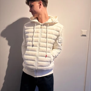 Vit pufferjacka från Moncler - Säljer en snygg vit pufferjacka från Moncler. Jackan har en dragkedja framtill och en mysig huva. Den är perfekt för kyliga dagar och har en stilren design med Moncler-loggan på ärmen. Passar både till vardags och lite finare tillfällen. Nfc funkar🔥