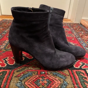 Svarta mocka stövletter med klack - Säljer ett par eleganta svarta stövletter i mocka med en snygg klack. De har en praktisk dragkedja på sidan för enkel på- och avtagning. Perfekta för höst och vinter, och de ger en stilren touch till vilken outfit som helst. Tillverkade i Spanien med äkta läder.