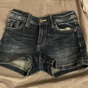Mörkblå jeansshorts från H&M - Säljer ett par mörkblå jeansshorts från H&M i storlek EUR 134. De har en klassisk femficksdesign med slitna detaljer och knappstängning. Perfekta för sommardagar eller en avslappnad stil. Passar bra till en enkel t-shirt eller linne.