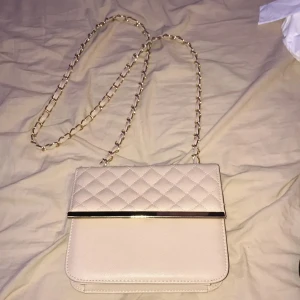 Beige quiltad axelväska - Säljer en superfin gräddvit axelväska med quiltat mönster. Väskan har en elegant kedjerem och en stilren metallkant. Perfekt för både vardag och fest! 💖