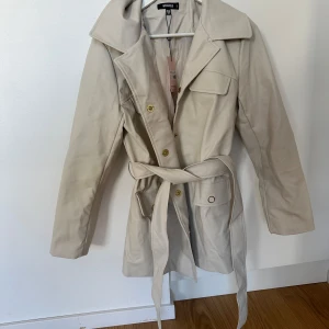 ”Skinnkappa” MISSGUIDED - Storlek 38, oanvänd och prislapp kvar.  Beige med snöre runt mage/midja