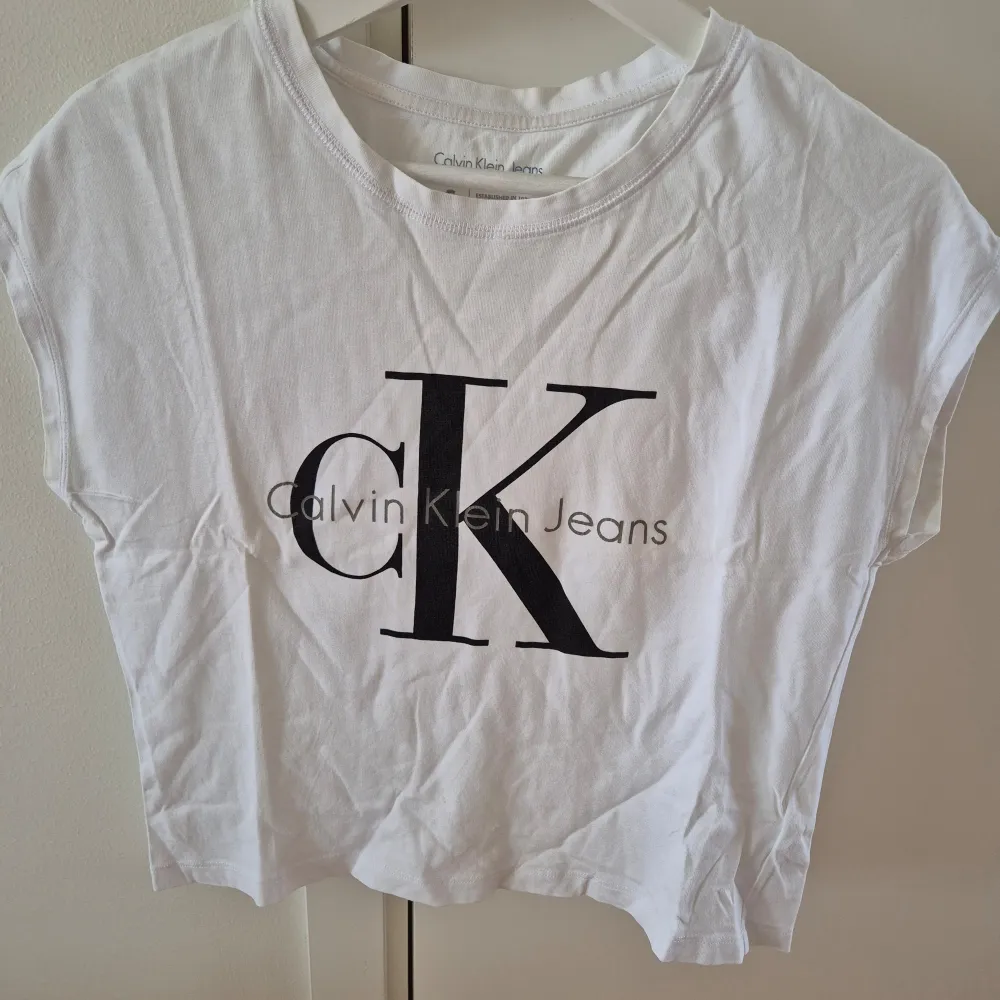 Vit T-shirt med svart/grå tryck från Calvin Klein. Lös modell. Storlek S. 100% bomull. Det är 3 st små stygn vid magen pga små hål. . T-shirts.