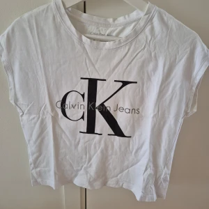 Tshirt CK - Vit T-shirt med svart/grå tryck från Calvin Klein. Lös modell. Storlek S. 100% bomull. Det är 3 st små stygn vid magen pga små hål. 