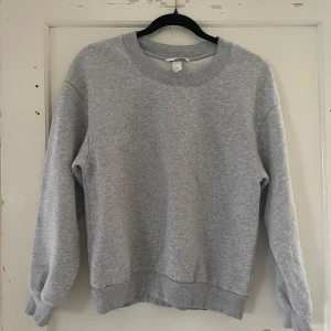 Grå sweatshirt med tryck från Off Black - Säljer en grå sweatshirt från Off Black i storlek S. Tröjan har ett tryck med texten 'OFF BLACK' på ryggen. Den är långärmad och gjord i ett mjukt och bekvämt material, perfekt för vardagsbruk. Passar bra till både jeans och mjukisbyxor!