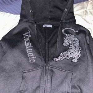 Svart hoodie med tigerbroderi - Säljer en svart hoodie från Von Studio. Hoodien har dragkedja och är perfekt för en avslappnad stil. Den är i bra skick och ger en skön stil. Storlek S men passar även M
