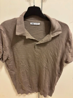Beige kortärmad polotopp från Zara - Säljer en beige kortärmad polotopp från Zara. Toppen har klassisk krage, knappar framtill och är tillverkad i ett mjukt, tunt material som känns skönt mot huden. Perfekt till jeans för en clean och enkel look.
