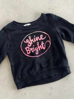 Svart sweatshirt Shine Bright H&M - Cool svart sweatshirt från H&M med trycket 'Shine Bright' i rosa på bröstet. Tröjan har rund halsringning och långa ärmar. Perfekt för en avslappnad och trendig look.