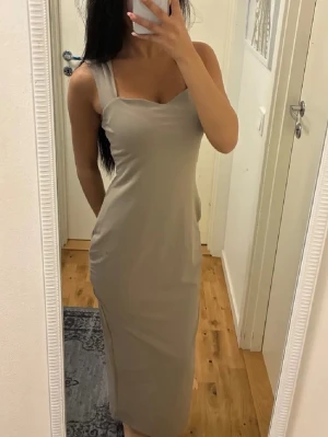 Beige långklänning med breda axelband - Säljer en stilren beige långklänning med breda axelband och figurnära passform. Klänningen har en enkel, elegant design utan mönster och är tillverkad i ett mjukt, stretchigt material som formar sig snyggt efter kroppen. Perfekt för dig som gillar minimalistisk stil.