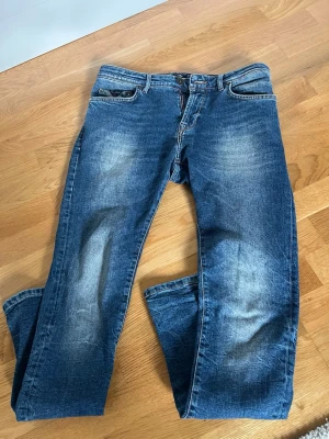 Blå raka jeans - Säljer ett par klassiska blå jeans med raka ben och snygga slitningar på låren. Jeansen har fem fickor, knappgylf och en cool tvättad look. Perfekta för en avslappnad stil och passar till det mesta. Materialet är denim i bomull. 30/32