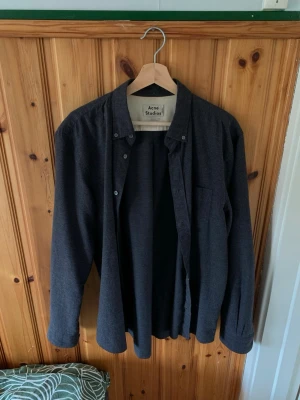 Mörkgrå skjorta från Acne Studios - Snygg mörkgrå skjorta från Acne Studios i mjuk bomull. Klassisk rak passform (classic fit) med långa ärmar och knappar framtill. Perfekt till jeans eller chinos för en clean look.