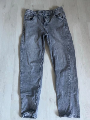 Grå raka jeans i denim - Säljer ett par grå jeans i klassisk rak modell med fem fickor och dragkedjegylf. Jeansen är tillverkade i denim och har en avslappnad passform. Perfekta för en stilren och enkel look.