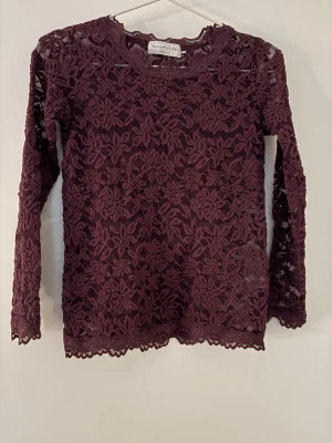 Vinröd spetsblus från Rosemunde - Vinröd långärmad blus från Rosemunde i genombruten spets med blommigt mönster. Blusen har rund halsringning och fina spetsdetaljer vid ärmslut och nederkant. Perfekt för dig som gillar romantisk och trendig stil.