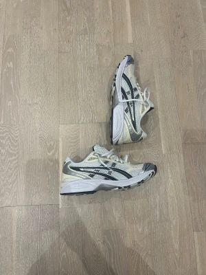 ASICS vita och beige sneakers - Snygga sneakers från ASICS i vitt och beige med svarta detaljer. Skorna har klassisk mesh-ovandel för bra andningsförmåga och silvriga inslag. Perfekta för en sportig och trendig look med tydlig retrovibe.