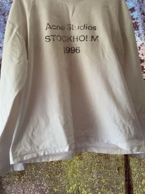 Vit långärmad t-shirt Acne Studios - Vit långärmad t-shirt från Acne Studios med tryck 'STOCKHOLM 1996' på bröstet. Klassisk passform och rund halsringning. Perfekt för en clean och stilren look.
