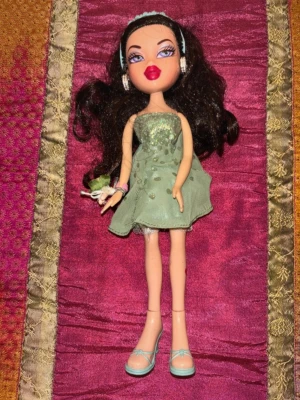 Vintage Bratz-docka i glittrig grön klänning – Y2K / tidigt 2000-tal - Original Bratz-docka från tidigt 2000-tal med klassisk glamorös Y2K-look. Dockan har långt mörkt hår, markerade Bratz-drag och bär en glittrig ljusgrön klänning med matchande skor och accessoarer.  Dockan är i mycket fint vintage-skick med välbevarat ansikte, hår och kropp. Klänningen har fina glittriga detaljer och accessoarer enligt bilderna ingår.  Perfekt för samlare, nostalgiker eller dig som älskar Bratz, Barbiecore och Y2K-estetik.  Skick: Mycket bra Märke: Bratz (MGA) Era: tidigt 2000-ta