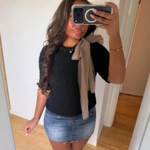 Svart blus med beige rosett - Säljer denna jättefina stickade toppen med en beige rosett på axeln. Man knyter rosetten själv så man kan justera hur stor den är💖