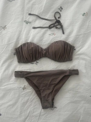 Brun bandeau bikini med rynkade detaljer - Snygg brun bandeau bikini med rynkade detaljer på överdelen och avtagbara axelband. Säljer endast överdelen!!! Finns ingen lapp den är bortklippt men är säker på storlek M🤗
