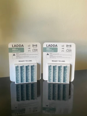 IKEA LADDA AA 2450mAh batterier - Två förpackningar med IKEA LADDA AA-batterier, 2450mAh. Batterierna är uppladdningsbara och kommer i en ljusgrå färg med vit text. Perfekta för elektronikprylar som fjärrkontroller, kameror eller spelkontroller.