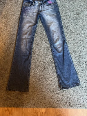 Lågmidjade jeans  - Crazy age jeans med bootcut, detaljer i rosa med låg midja. Ett litet hål vid ena fotknölen plus lätt heelbite men annars hela. 