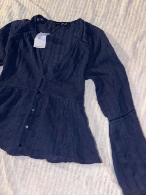 Mörkblå blus från Stradivarius - Snygg mörkblå blus från Stradivarius med knappar framtill och v-ringning. Blusen har långärmad design och är tillverkad i ett lätt, strukturerat material som ger en avslappnad och trendig look. Helt ny och oanvänd