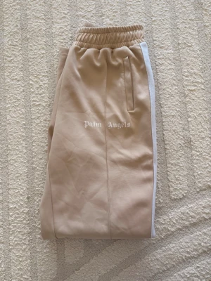 Beige mjukisbyxor Palm Angels - Snygga beige mjukisbyxor från Palm Angels med vita och svarta sidoremsor. 