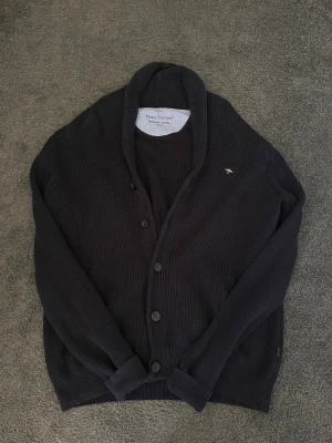 Mörkblå kofta från Fynch-Hatton - Kofta i mörkblått från Fynch-Hatton, tillverkad i supersoft bomull. Modellen har ribbstickad struktur, knäppning framtill med tre knappar och en liten broderad logga på bröstet. Perfekt för lager-på-lager och chill stil.