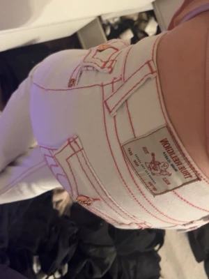 Vita True Religion jeans med rosa sömmar - Jätte fina vita true Religion jeans, med fina detaljer. Har andvänt dom 1 gång tidigare och säljer dom nu för att dom inte har kommit till andvändning
