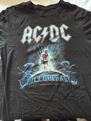 Svart AC/DC Ballbreaker t-shirt - Cool svart t-shirt med stort AC/DC-tryck och motiv från Ballbreaker-albumet. T-shirten har klassisk passform, rund hals och korta ärmar. Perfekt för dig som gillar rock och vill sticka ut med en ikonisk bandtröja. XL men passar L också.