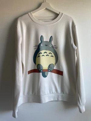 Vit sweatshirt med Totoro-tryck - Säljer en vit sweatshirt med ett stort tryck av Totoro från Studio Ghibli på framsidan. Tröjan har rund halsringning och långa ärmar. Perfekt för dig som gillar anime. OBS, varan har tecken på användning: se bild 2.