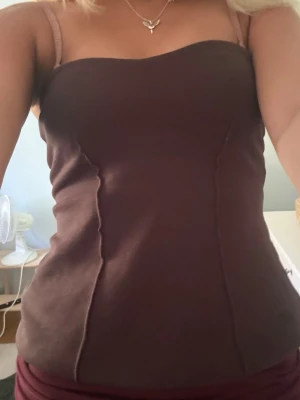 Brun bandeau topp med sömdetaljer - Säljer en brun bandeau topp med snygga sömdetaljer framtill. Toppen har en figurnära passform och är axelbandslös, perfekt för att skapa en trendig look. Materialet ser ut att vara stretchigt och bekvämt.använd 1 gång