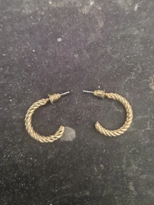 Guldpläterade tvinnade hoops örhängen - Säljer ett par snygga guldpläterade hoops med tvinnad design. Örhängena är halvcirkelformade och har en stilren, klassisk look som passar till många outfits. Perfekta för dig som gillar tidlösa accessoarer med lite extra detalj.