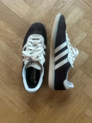 Adidas Samba OG  - Klassiska Adidas Samba OG sneakers i brun och vitt med de ikoniska tre ränderna på sidan och gummisula. 
