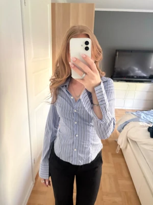 Blåvit randig skjorta med knappar - Snygg blå och vit randig skjorta med klassisk krage och långa ärmar. Skjortan har vita knappar framtill och är figursydd för en stilren look. Perfekt till jeans eller kostymbyxor.