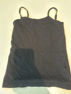 Svart linnetopp från Basic You - En enkel svart linnetopp från Basic You i ekologisk bomull. Toppen har smala axelband och rak passform, perfekt för en avslappnad och stilren look. Passar bra till jeans eller shorts.