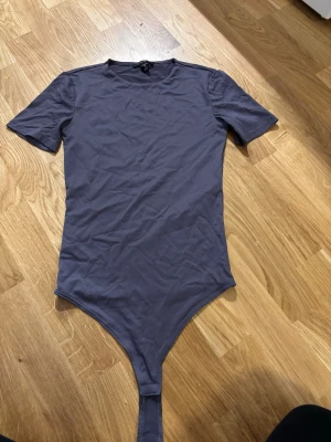Lila kortärmad body - En enkel och stilren lila body med korta ärmar och rund hals. Bodyn har en klassisk passform och knäppning i grenen. Perfekt att styla till både jeans och kjol. Materialet känns mjukt och stretchigt för en bekväm känsla.