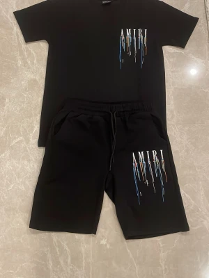 Amiri shorts t shirt  - Svart t-shirt från Amiri med korta ärmar och rund hals. På bröstet finns ett tryck med Amiri-loggan och färgstänk i blått, gult och rött. Tillverkad i mjuk bomull för en skön och avslappnad stil.