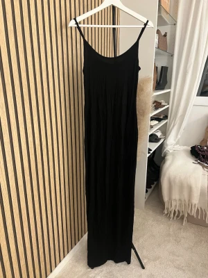 Svart långklänning med smala axelband - En stilren svart långklänning med smala axelband och rundad urringning. Klänningen har en rak och enkel passform som ger en tidlös look. Perfekt att styla med accessoarer för en personlig touch. Skriv om ni vill ha bild på 🫶🏼🫶🏼