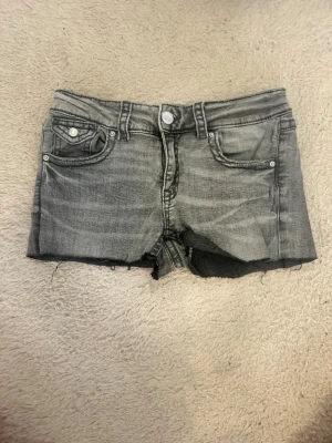 Grå jeansshorts - Grå jeansshorts från Gina Tricot. Shortsen har knapp och dragkedja framtill samt bakfickor med knappdetalj.