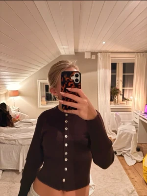 Mörklila kofta med pärlemorknappar - Snygg mörklila kofta med långa ärmar och pärlemorskimrande knappar hela vägen framtill. Figurnära passform och klassisk rund halsringning. Perfekt att styla till jeans eller kjol.