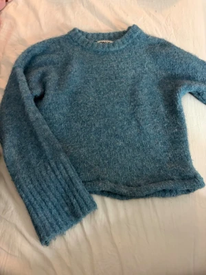 Blå fluffig stickad tröja från ONLY - Mysig blå stickad tröja från ONLY med fluffig textur. Tröjan har rund halsringning, långa ärmar och ribbstickade muddar. Perfekt för att hålla värmen under kyliga dagar.