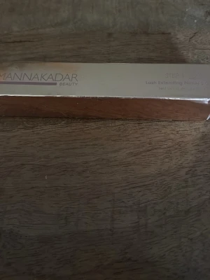 Manna Kadar Lash Extending Primer - Mascara primer från Manna Kadar Beauty i en stilren, rektangulär förpackning med metallicfinish. Produkten är designad för att ge extra längd och volym till fransarna innan mascara appliceras. Perfekt för dig som vill ha en intensivare franslook.