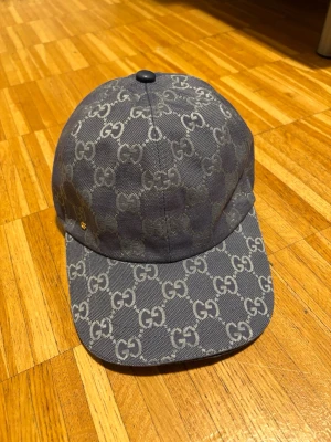 Grå G keps med GG-mönster - Snygg grå keps från G med klassiskt GG-mönster över hela kepsen. Materialet är canvas med ljus insida och justerbar rem bak. Perfekt för dig som vill ha en exklusiv och trendig accessoar.