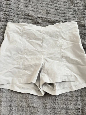 Vita högmidjade shorts i bomull - Snygga vita högmidjade shorts i bomull med enkel och stilren design. Perfekta för varma dagar och lätta att matcha med olika toppar. Klassisk passform utan synliga detaljer eller fickor.