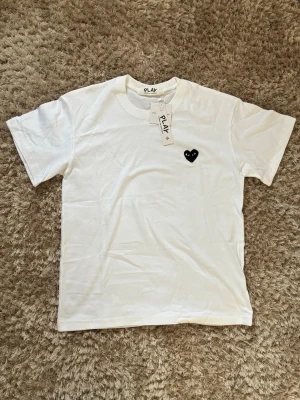 Vit Comme des Garçons Play t-shirt - Vit t-shirt från Comme des Garçons Play med det ikoniska svarta hjärtat med ögon broderat på bröstet. Klassisk rund halsringning och korta ärmar. Tillverkad i mjuk bomull och har märkets taggar kvar.