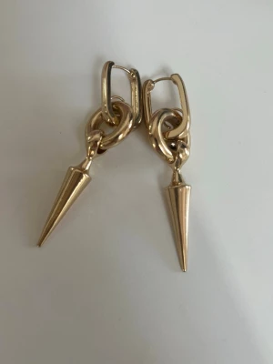  örhängen  - Snygga örhängen i guldfärgad metall med coola konformade hängen. De har en modern design med runda länkar och spetsiga detaljer som ger en edgy känsla. Perfekta för att lyfta din stil med en trendig touch.