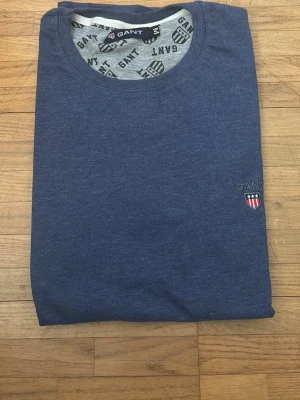 Blå t-shirt från GANT med logga - Snygg marinblå t-shirt från GANT med rund halsringning och broderad logga på bröstet. Tillverkad i mjuk bomull som känns skön mot huden. Perfekt för dig som gillar klassisk och stilren design.