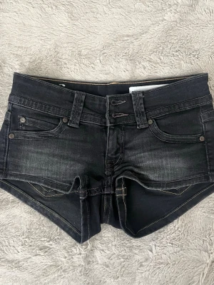 Svarta denimshorts med fickor - Snygga svarta denimshorts med fem fickor, bälteshällor och slitna detaljer. Klassisk jeanslook med knapp- och dragkedjestängning. Perfekta för varma dagar och en avslappnad stil.