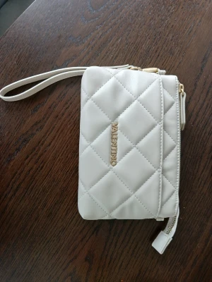 Vit quiltad clutch från Valentino - Snygg vit clutch (19 × 13 cm) från Valentino i quiltat mönster med guldfärgade detaljer och dragkedja. har handledsrem och flera fack