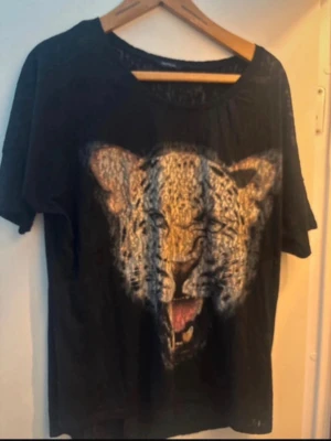 Svart t-shirt med leopardtryck Lindex - Cool svart t-shirt från Generous by Lindex med ett stort leopardtryck framtill. T-shirten har rund halsringning och korta ärmar. Perfekt för dig som vill sticka ut med ett djurmotiv.